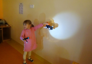 Dziewczynka trzyma w ręku włączoną latarkę skierowaną na auto.